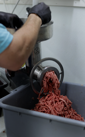 a worker stands near a giant meat grinder turning beef into hamburger